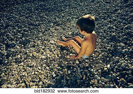 High angle view of boy sitting on rocky beach View Large Photo Image Stock Image - High angle view of boy sitting on rocky beach. Fotosearch