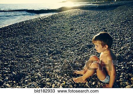 High angle view of boy sitting on rocky beach View Large Photo Image Stock Image - High angle view of boy sitting on rocky beach. Fotosearch
