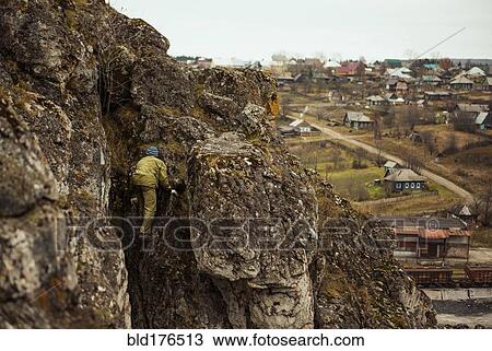 Stock Image - Hiker climbing rocky mountainside. Fotosearch