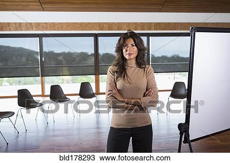 Stock Image - Hispanic businesswoman standing in meeting room. Fotosearch