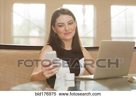 Stock Photography - Hispanic businesswoman using cell phone in office. Fotosearch