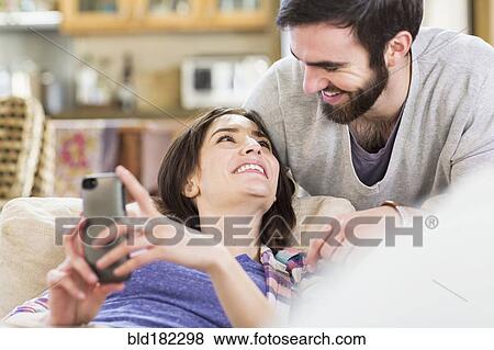 Hispanic couple using cell phone on sofa View Large Photo Image Stock Photo - Hispanic couple using cell phone on sofa. Fotosearch