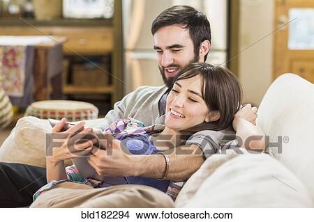 Picture - Hispanic couple using digital tablet on sofa. Fotosearch