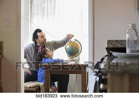 Stock Image - Hispanic father and daughter examining globe. Fotosearch
