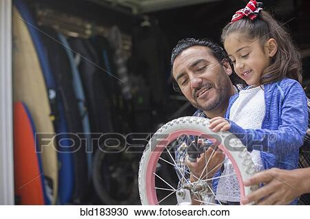 Stock Image - Hispanic father teaching daughter to repair bicycle. Fotosearch