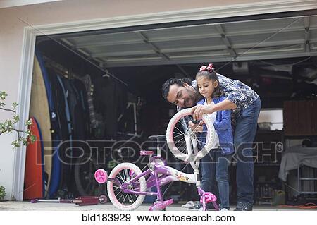 Stock Photo - Hispanic father teaching daughter to repair bicycle. Fotosearch