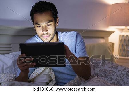 Stock Photograph - Hispanic man using digital tablet in bed. Fotosearch