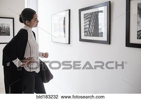 Stock Image - Hispanic woman admiring art in gallery. Fotosearch