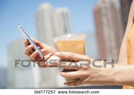 Stock Photo - Hispanic woman holding cell phone and iced coffee. Fotosearch