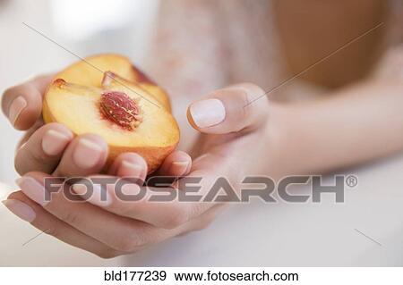 Stock Photo - Hispanic woman holding halved peach. Fotosearch