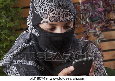 Stock Photo - Hispanic woman in headscarf using cell phone. Fotosearch