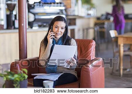 Stock Image - Hispanic woman paying bills on cell phone in cafe. Fotosearch