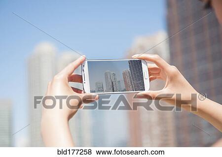 Stock Photo - Hispanic woman photographing skyline with cell phone. Fotosearch