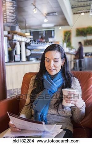 Picture - Hispanic woman reading paperwork in cafe. Fotosearch