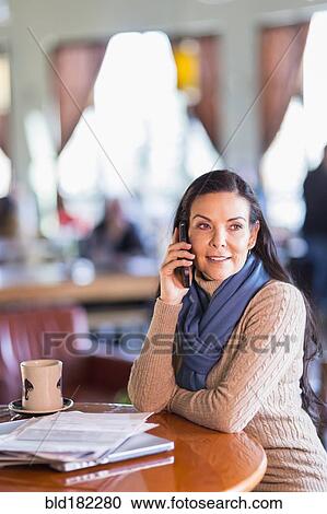Stock Image - Hispanic woman talking on cell phone in cafe. Fotosearch