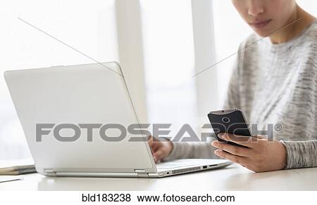 Stock Photo - Hispanic woman using cell phone and laptop. Fotosearch