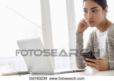 Stock Photo - Hispanic woman using cell phone and laptop. Fotosearch