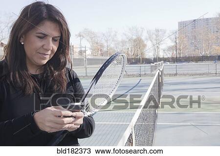 Stock Image - Hispanic woman using cell phone on tennis court. Fotosearch