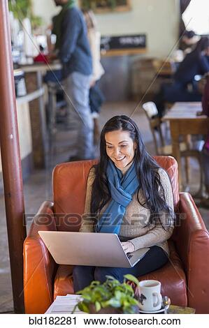 Stock Image - Hispanic woman using laptop in cafe. Fotosearch