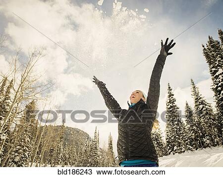 Stock Image - Low angle view of Caucasian woman playing in snow. Fotosearch