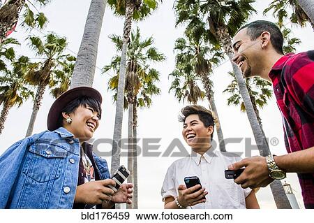 Stock Photo - Low angle view of friends using cell phones outdoors. Fotosearch