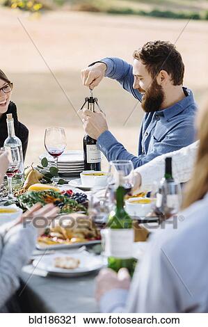Man opening bottle of wine at outdoor table View Large Photo Image Stock Image - Man opening bottle of wine at outdoor table. Fotosearch