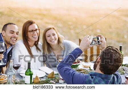 Man photographing friends at outdoor table View Large Photo Image Stock Image - Man photographing friends at outdoor table. Fotosearch