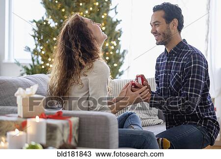 Stock Image - Man proposing to girlfriend on sofa. Fotosearch