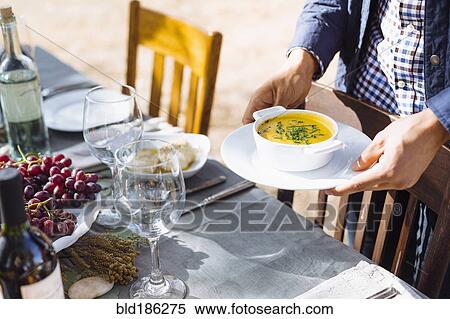 Stock Photography - Man setting platter of soup on outdoor table. Fotosearch