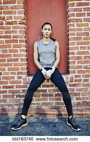 Stock Image - Mixed race athlete sitting on brick wall. Fotosearch