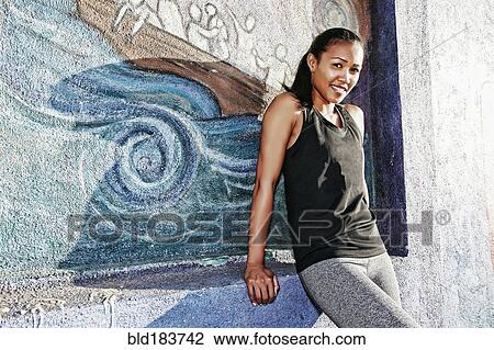Stock Image - Mixed race athlete sitting on mural wall. Fotosearch