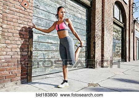 Stock Image - Mixed race athlete stretching on sidewalk. Fotosearch