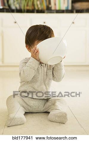 Stock Image - Mixed race baby boy drinking from bowl on floor. Fotosearch