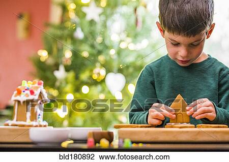 Stock Image - Mixed race boy building gingerbread house. Fotosearch