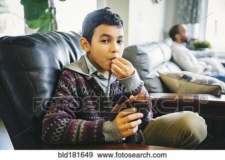 Stock Photo - Mixed race boy eating in armchair. Fotosearch