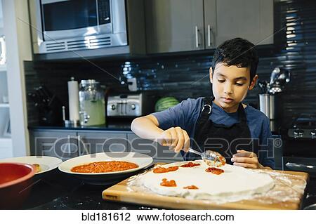 Stock Image - Mixed race boy making pizza in kitchen. Fotosearch