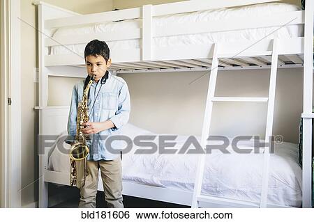 Stock Photograph - Mixed race boy playing saxophone in bedroom. Fotosearch