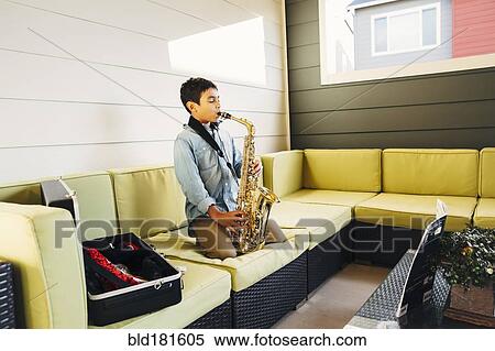 Stock Photography - Mixed race boy playing saxophone on sofa. Fotosearch