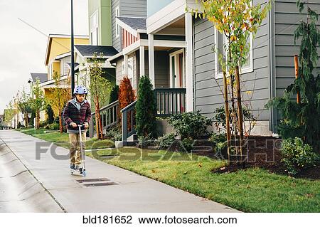 Stock Image - Mixed race boy riding scooter on sidewalk. Fotosearch