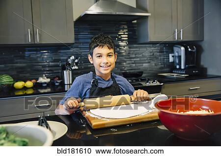 Stock Image - Mixed race boy rolling dough in kitchen. Fotosearch