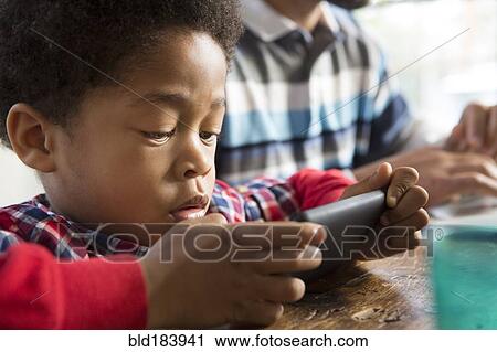 Mixed race boy using cell phone at table View Large Photo Image Stock Image - Mixed race boy using cell phone at table. Fotosearch
