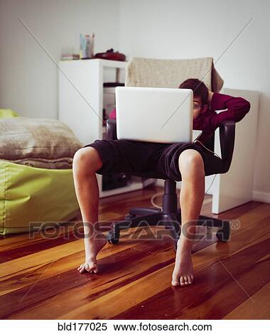 Stock Photography - Mixed race boy using laptop in chair. Fotosearch