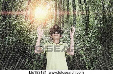 Stock Image - Mixed race boy wearing virtual reality goggles in remote forest. Fotosearch