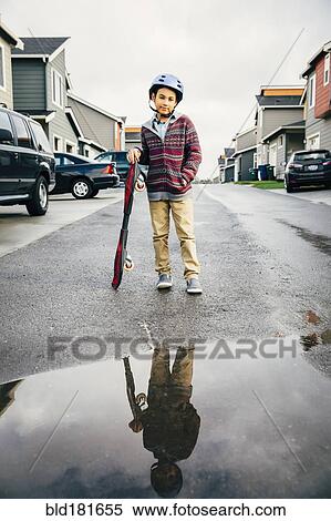 Stock Photography - Mixed race boy with skateboard reflected in puddle. Fotosearch