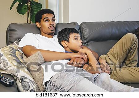 Stock Photo - Mixed race brothers watching television on sofa. Fotosearch