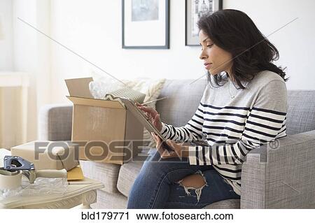 Stock Image - Mixed race business owner using digital tablet on sofa. Fotosearch