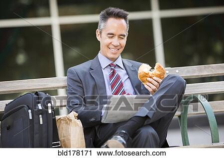 Stock Image - Mixed race businessman eating and using digital tablet. Fotosearch