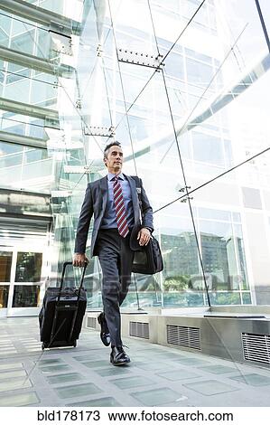 Mixed race businessman rolling luggage outdoors View Large Photo Image Stock Image - Mixed race businessman rolling luggage outdoors. Fotosearch