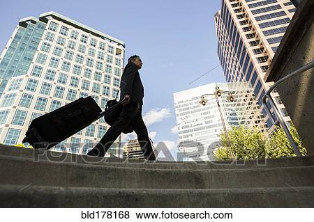 Mixed race businessman rolling luggage outdoors View Large Photo Image Stock Photo - Mixed race businessman rolling luggage outdoors. Fotosearch