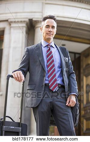 Mixed race businessman rolling luggage outdoors View Large Photo Image Stock Photo - Mixed race businessman rolling luggage outdoors. Fotosearch